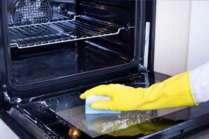mano con guanto giallo che pulisce forno