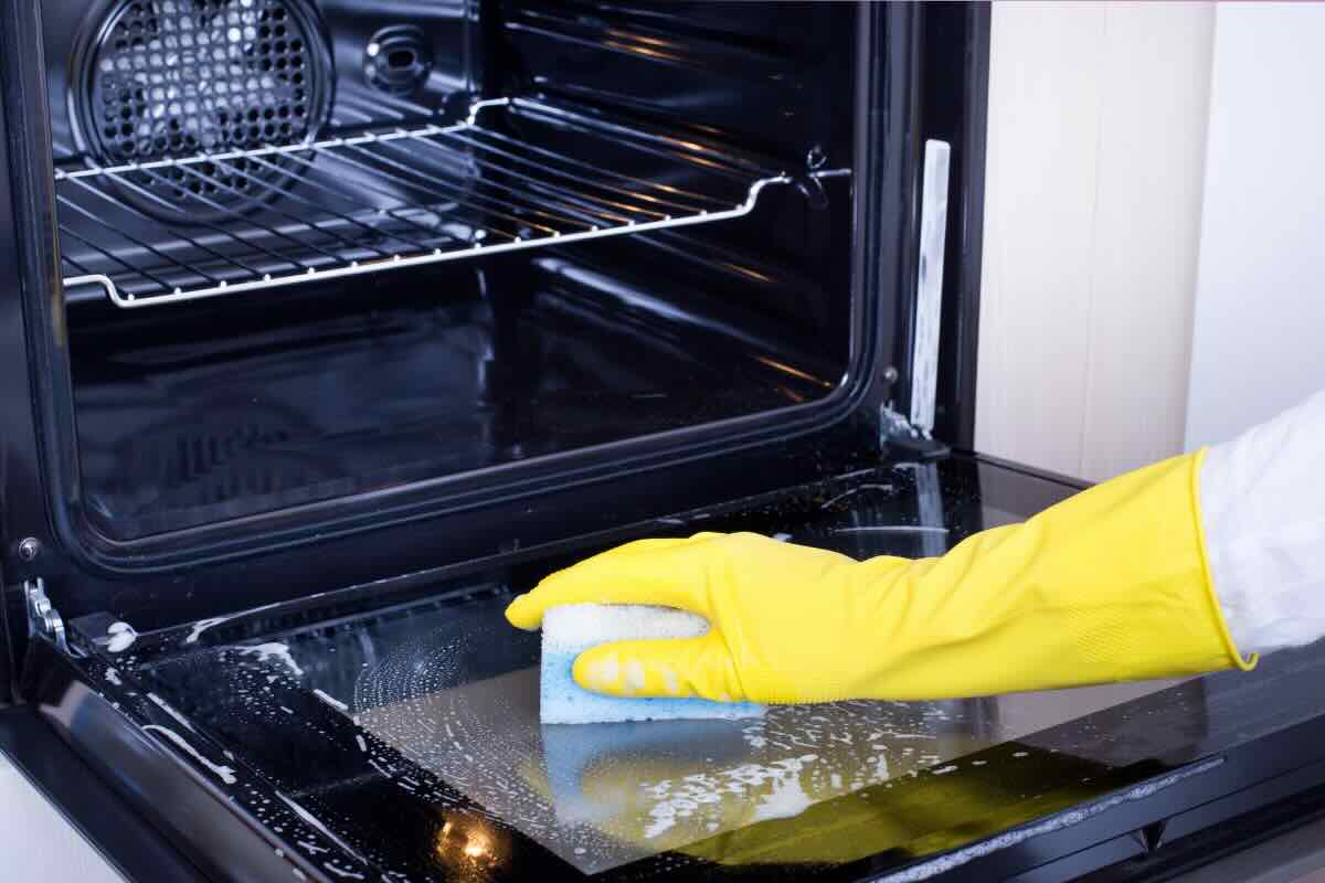 mano con guanto giallo che pulisce forno