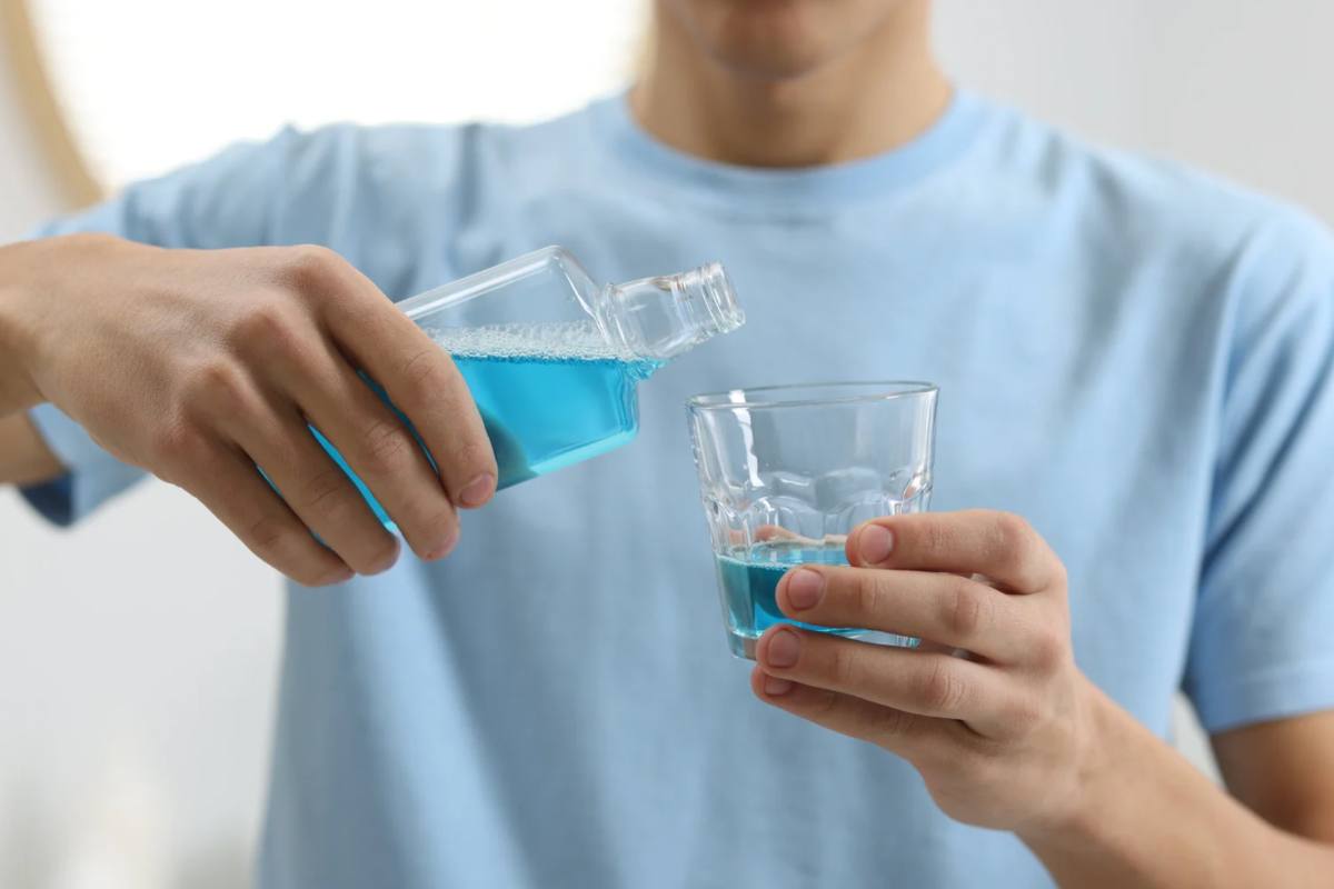 Uomo che versa colluttorio azzurro in un bicchiere