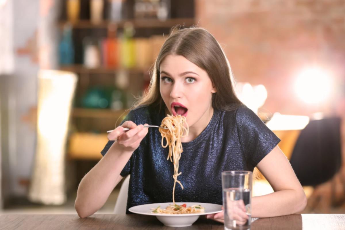 donna seduta al tavolo che mangia un piatto di spaghetti