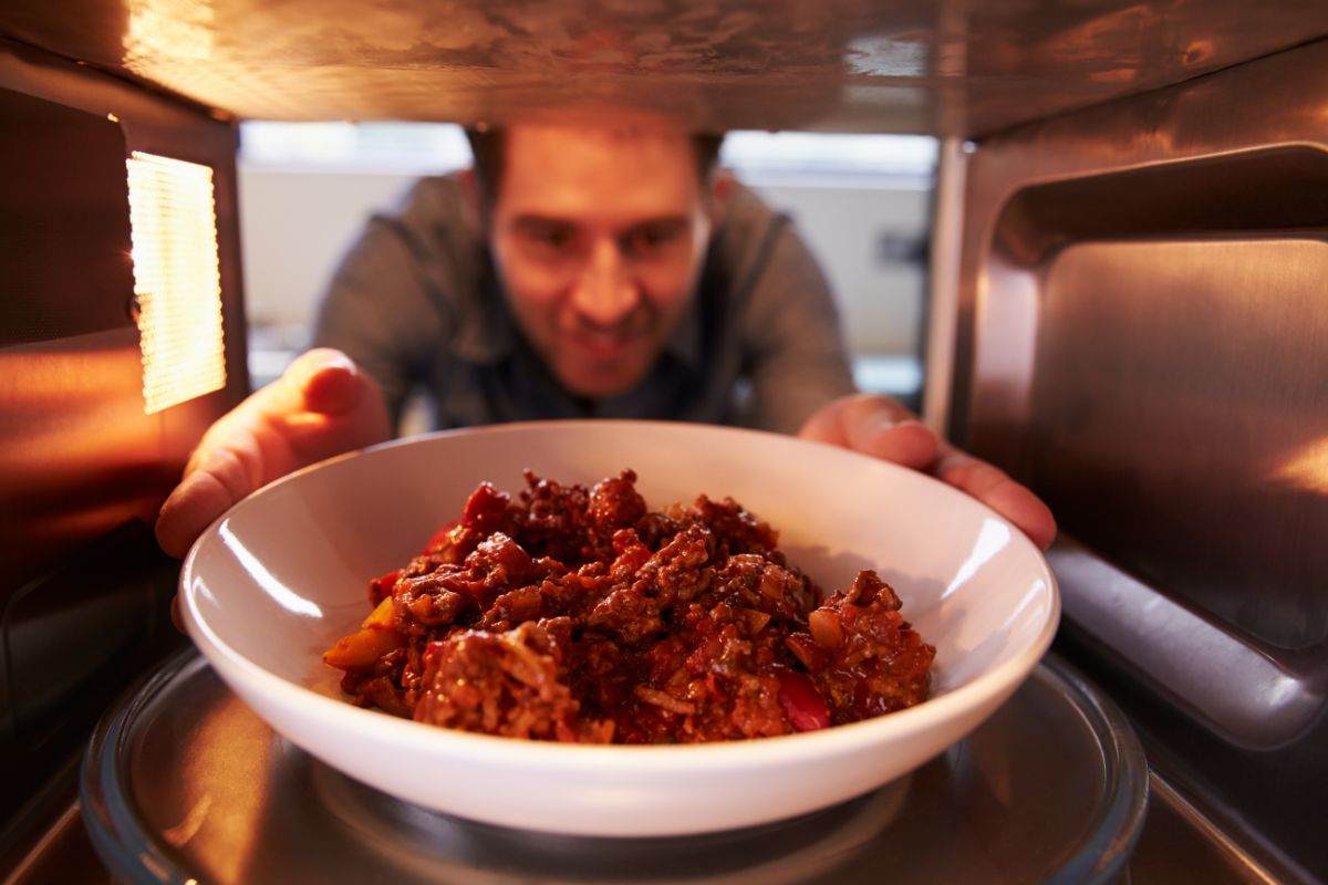 uomo che mette un piatto di pasta nel microonde 