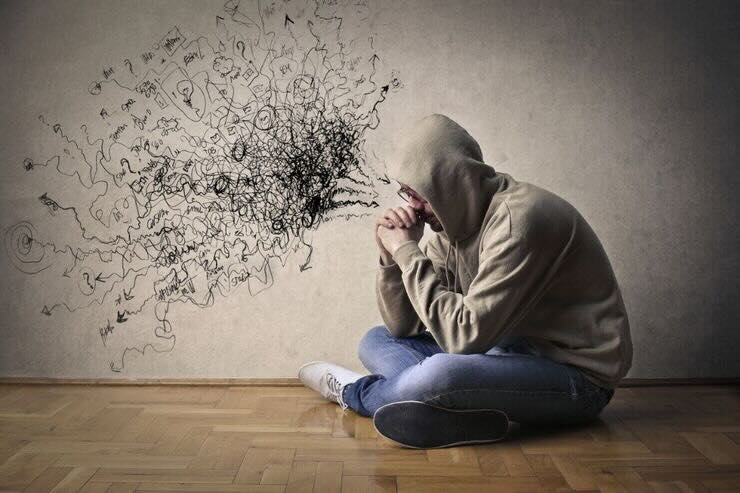 Ragazzo seduto si tiene il viso con le mani, sul muro sono disegnati tanti ghirigori con la penna 
