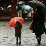 Madre e figlia che camminano in strada con ombrello