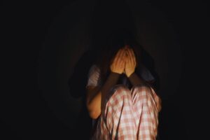Ragazza rannicchiata al buio si copre il volto per la paura
