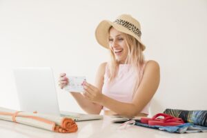 Donna al PC con telo da spiaggia accanto che tiene in mano un biglietto