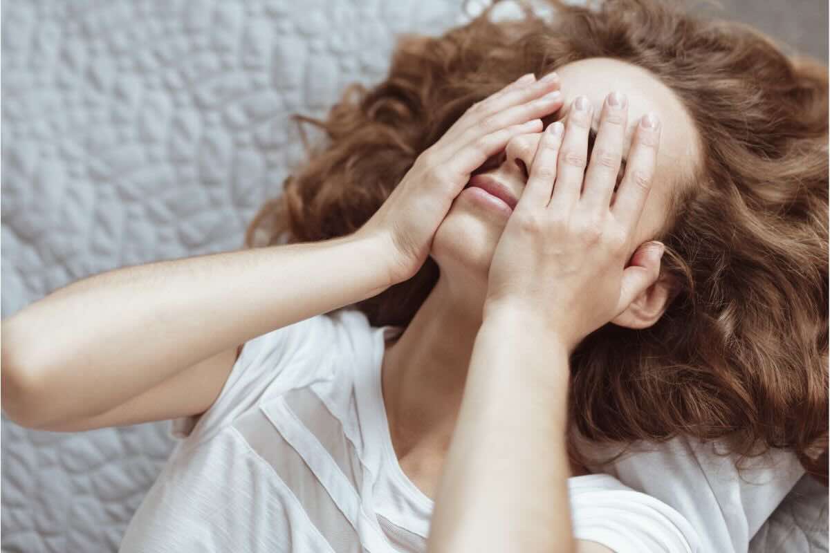 Ragazza affranta con mani sul viso sdraiata sul letto