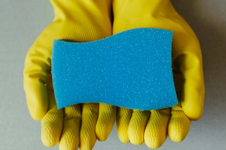 mani con guanti gialli e spugna azzurra
