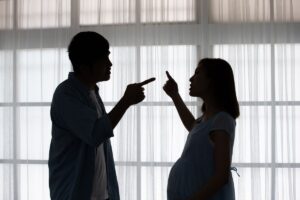 donna incinta e uomo in penombra entrambi si puntano dito contro